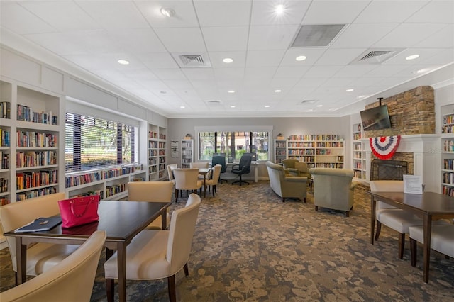 carpeted dining area with ornamental molding, a stone fireplace, and built in shelves