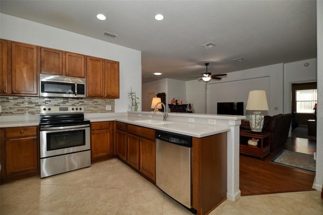 kitchen with a peninsula, appliances with stainless steel finishes, brown cabinetry, and a sink