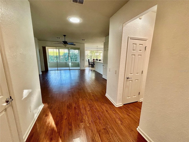 hallway with a textured wall, dark wood finished floors, visible vents, and baseboards