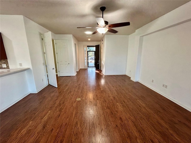 unfurnished living room featuring a textured ceiling, baseboards, dark wood finished floors, and a ceiling fan