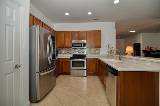 kitchen featuring brown cabinets, a peninsula, stainless steel appliances, light countertops, and a sink