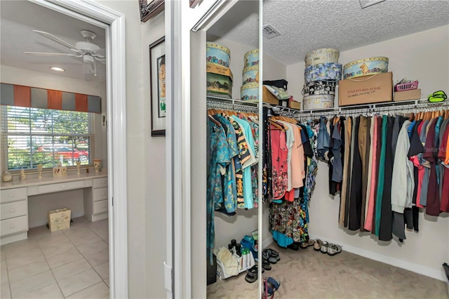 spacious closet featuring ceiling fan, built in desk, and light tile patterned floors