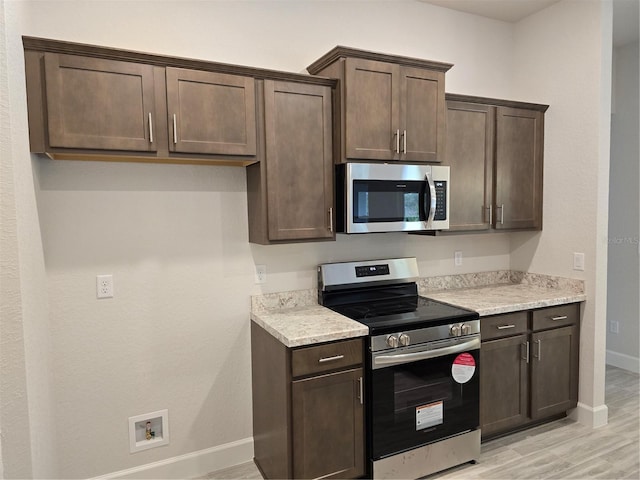 kitchen with dark brown cabinets, light hardwood / wood-style floors, and appliances with stainless steel finishes