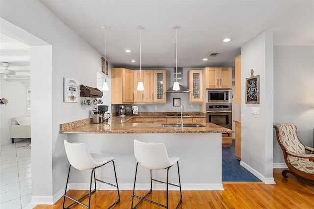 kitchen with decorative light fixtures, sink, kitchen peninsula, stainless steel appliances, and wall chimney range hood