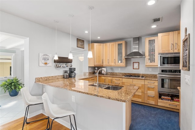 kitchen with wall chimney range hood, sink, appliances with stainless steel finishes, decorative light fixtures, and kitchen peninsula