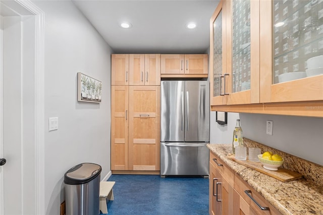 kitchen featuring stainless steel refrigerator, light brown cabinetry, and light stone countertops