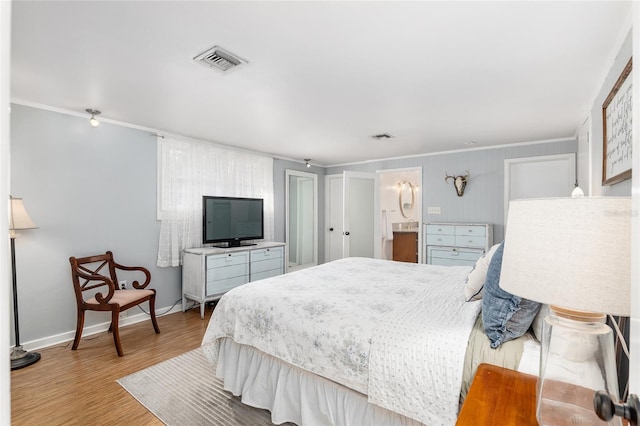 bedroom with ornamental molding, light wood-type flooring, and ensuite bath