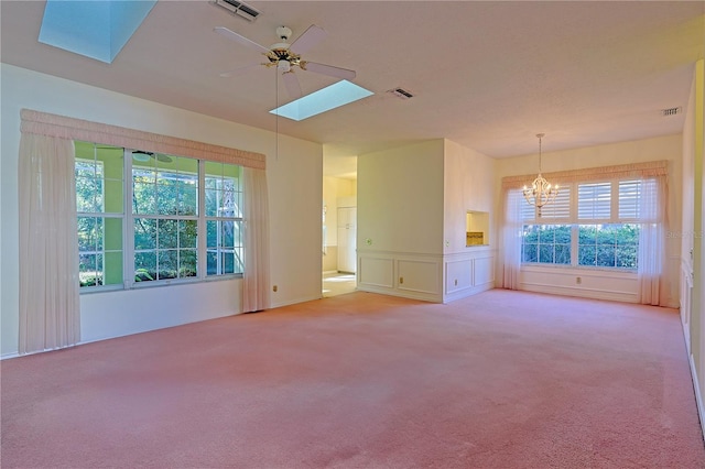 carpeted empty room featuring ceiling fan with notable chandelier and a skylight