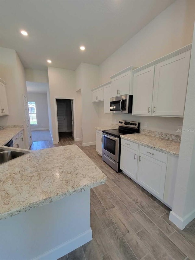 kitchen with white cabinetry, light stone countertops, stainless steel appliances, and light wood-type flooring