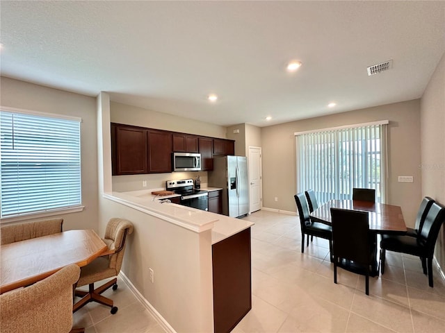 kitchen with appliances with stainless steel finishes, light tile patterned floors, dark brown cabinetry, and kitchen peninsula