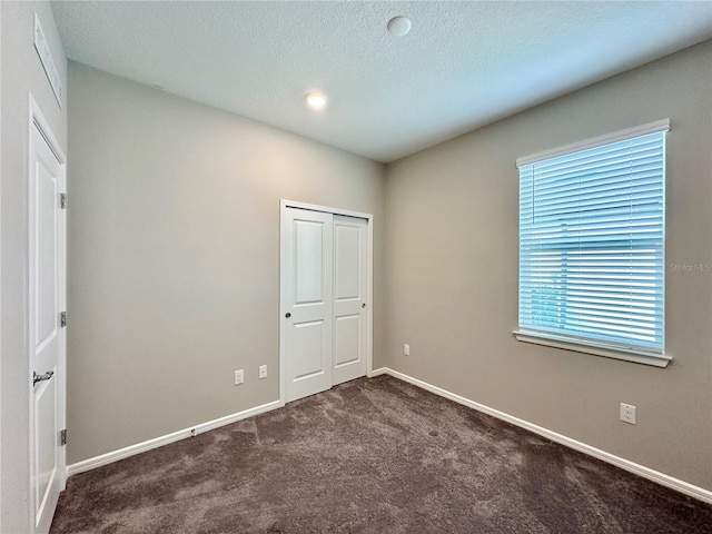 unfurnished bedroom featuring a textured ceiling, dark carpet, and a closet