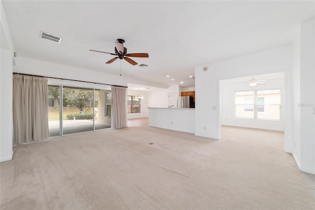 unfurnished living room featuring light carpet and ceiling fan with notable chandelier