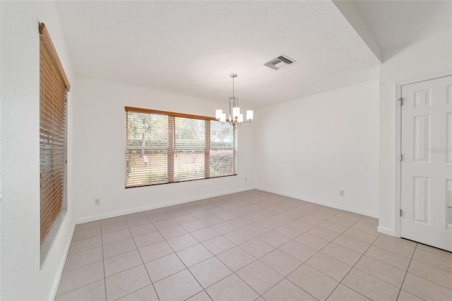 tiled empty room with an inviting chandelier and a textured ceiling