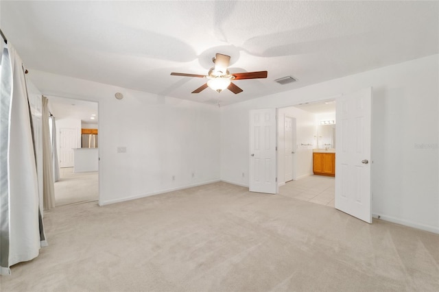 unfurnished bedroom with light carpet, ensuite bath, stainless steel refrigerator, and ceiling fan