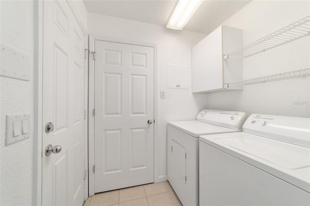 clothes washing area featuring cabinets, light tile patterned flooring, washing machine and clothes dryer, and a textured ceiling