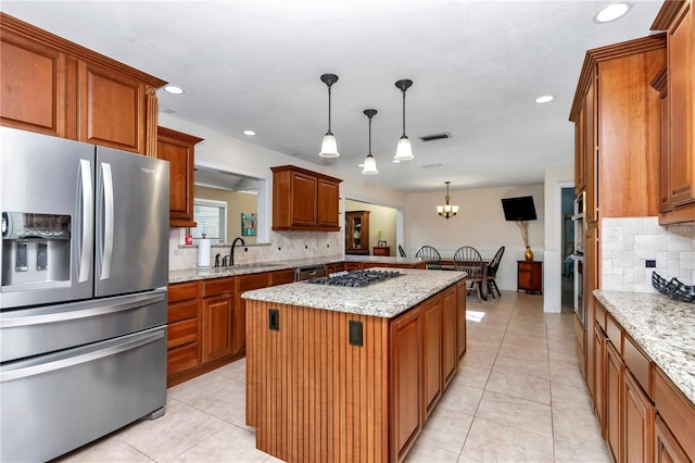 kitchen featuring sink, appliances with stainless steel finishes, hanging light fixtures, light stone countertops, and a kitchen island