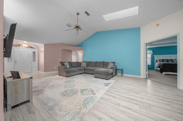 living room featuring lofted ceiling with skylight, light hardwood / wood-style floors, and ceiling fan