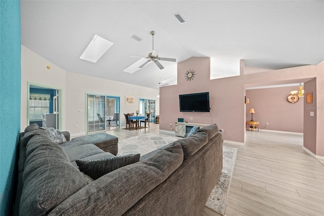 living room with ceiling fan, vaulted ceiling with skylight, and light wood-type flooring