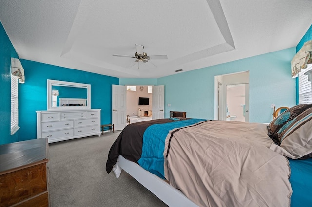 carpeted bedroom featuring a raised ceiling, connected bathroom, a textured ceiling, and ceiling fan