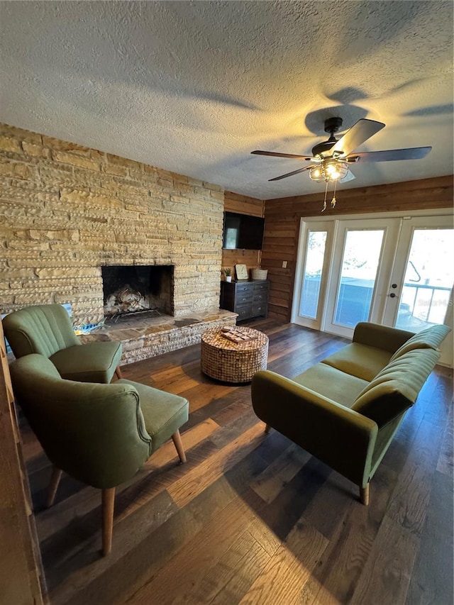 living room with ceiling fan, wooden walls, hardwood / wood-style floors, and a stone fireplace