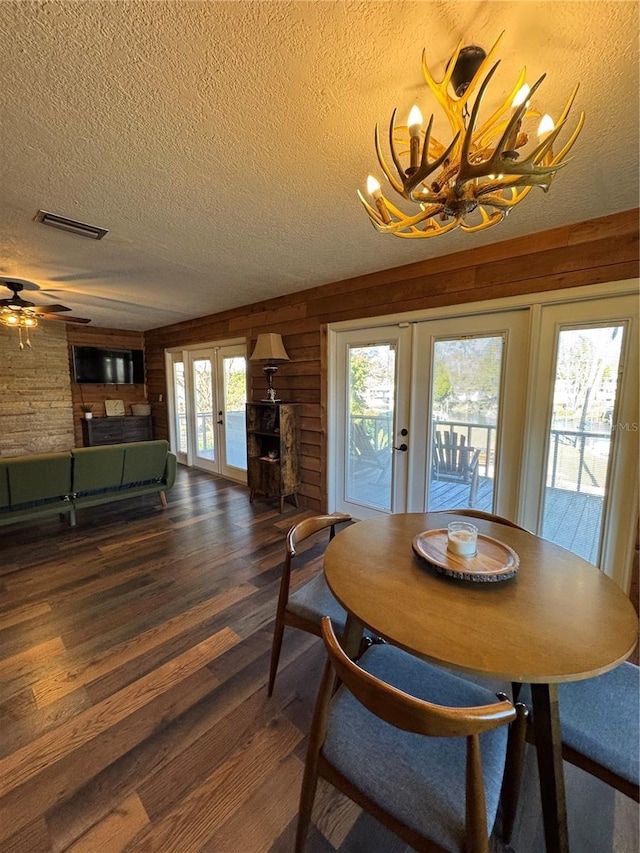 dining room featuring dark hardwood / wood-style floors, wood walls, a chandelier, a textured ceiling, and french doors