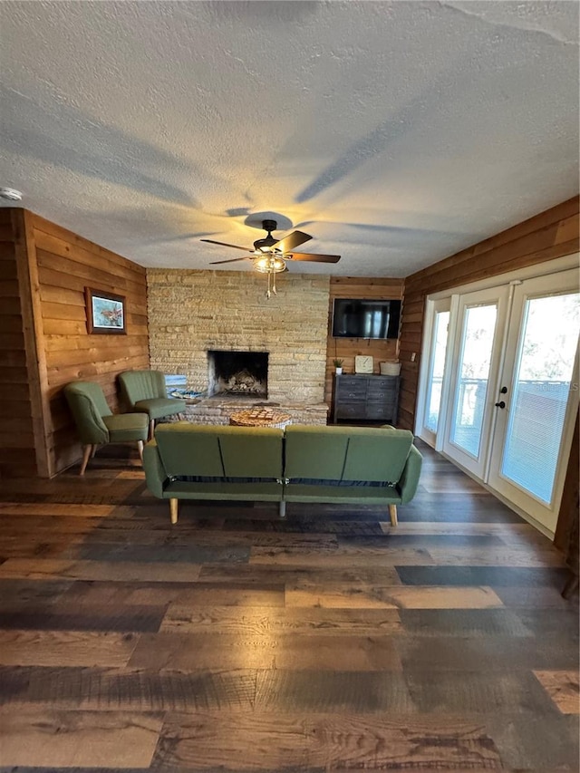 living room featuring a fireplace, wooden walls, ceiling fan, dark wood-type flooring, and a textured ceiling