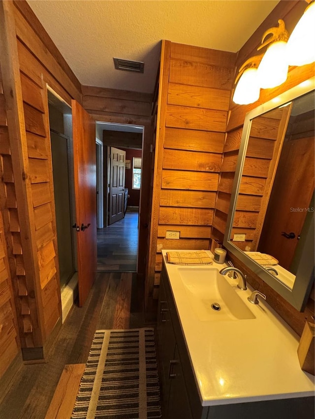 bathroom with wood-type flooring, vanity, a textured ceiling, and wood walls