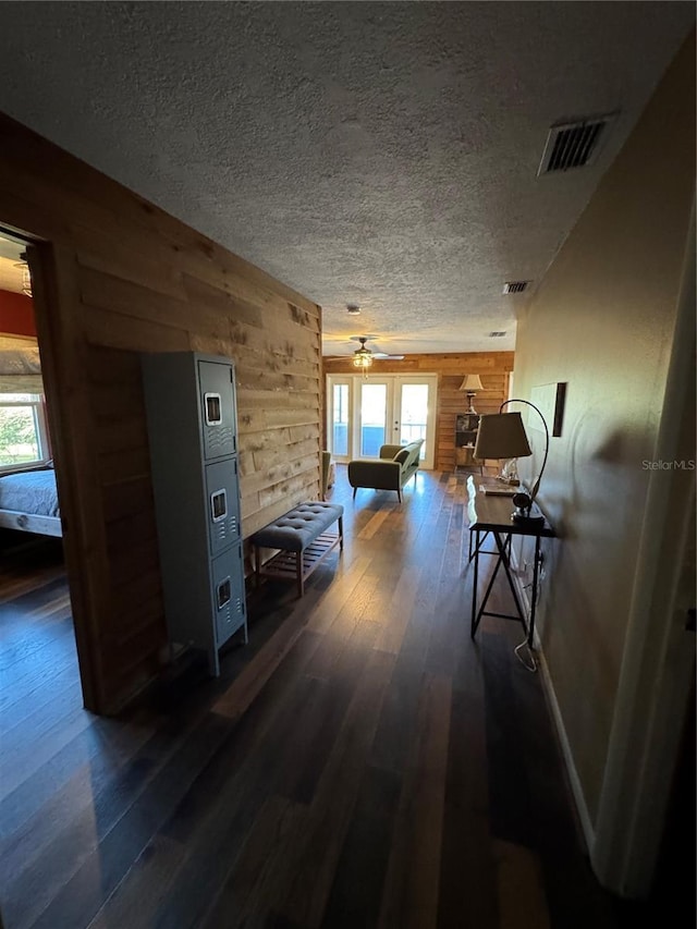 hallway featuring dark wood-type flooring, a textured ceiling, and wood walls