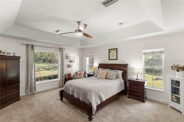 bedroom featuring a raised ceiling, light colored carpet, and ceiling fan