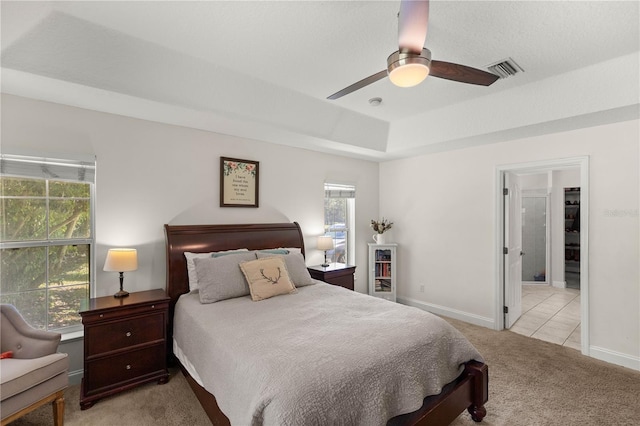 bedroom featuring multiple windows, light colored carpet, a raised ceiling, and ceiling fan