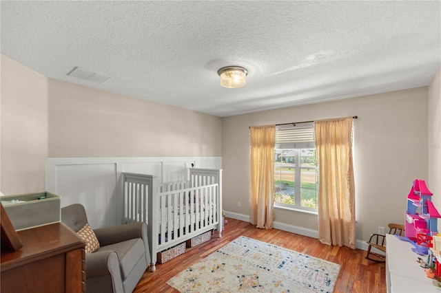 bedroom with a nursery area, hardwood / wood-style floors, and a textured ceiling