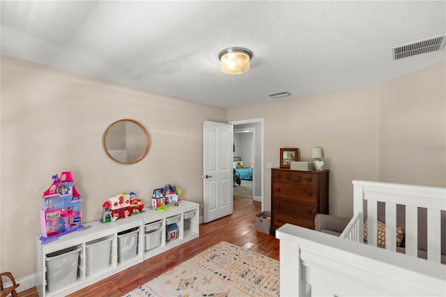 bedroom with wood-type flooring, a nursery area, and a textured ceiling
