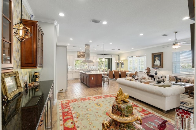 living area with light wood-style floors, recessed lighting, visible vents, and crown molding