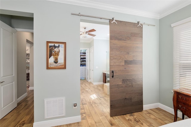 hall with ornamental molding, a barn door, visible vents, and light wood-style floors