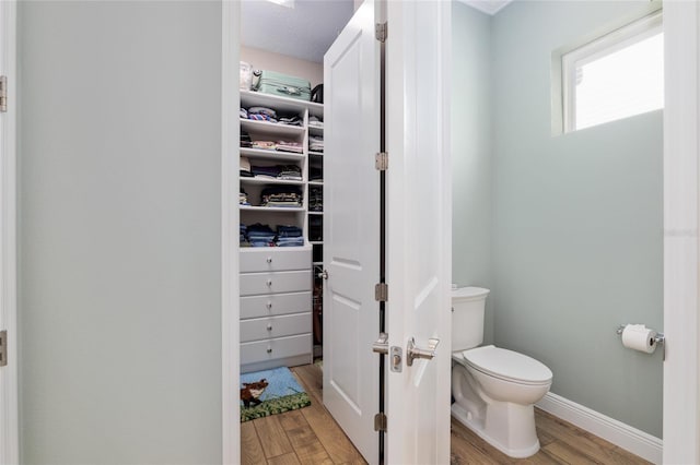 bathroom with toilet, a spacious closet, baseboards, and wood finished floors