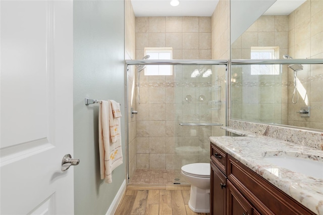 bathroom featuring wood finished floors, a shower stall, toilet, and vanity