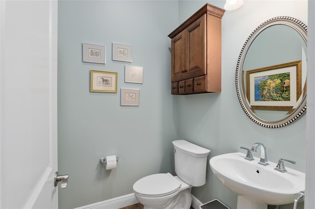 half bathroom featuring toilet, baseboards, and a sink