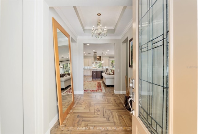 entryway with baseboards, a notable chandelier, a tray ceiling, and crown molding