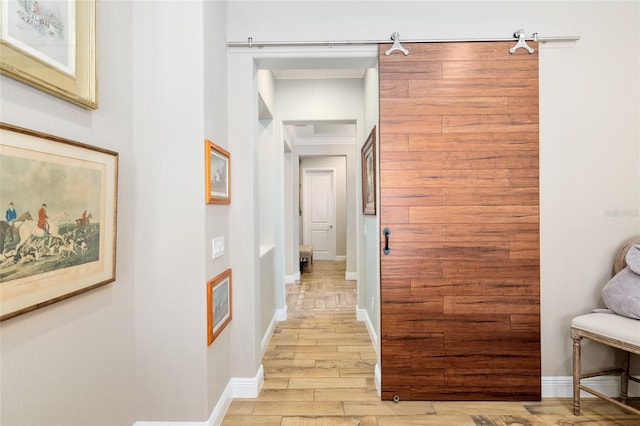 corridor featuring ornamental molding, light wood-type flooring, baseboards, and a barn door