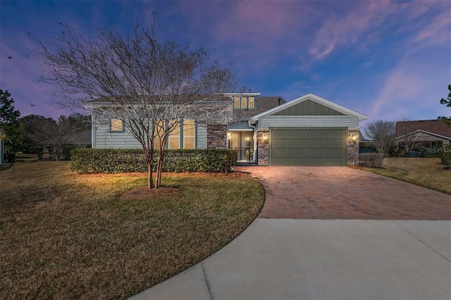 view of front facade with stone siding, an attached garage, decorative driveway, a yard, and board and batten siding