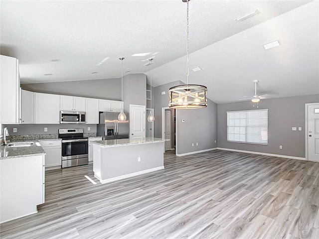 kitchen with light stone counters, a center island, appliances with stainless steel finishes, pendant lighting, and white cabinets