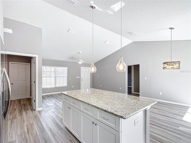 kitchen with light stone countertops, a center island, pendant lighting, and lofted ceiling