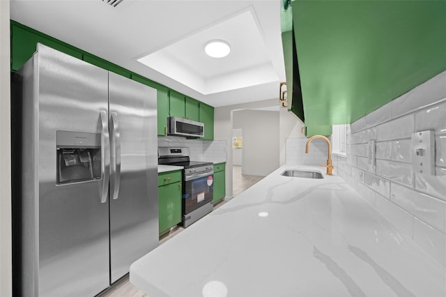 kitchen with green cabinetry, sink, a tray ceiling, stainless steel appliances, and light stone countertops