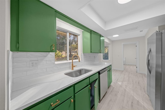 kitchen with sink, light stone counters, green cabinets, stainless steel appliances, and backsplash