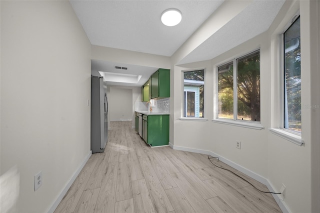 kitchen with sink, light hardwood / wood-style flooring, green cabinets, appliances with stainless steel finishes, and tasteful backsplash