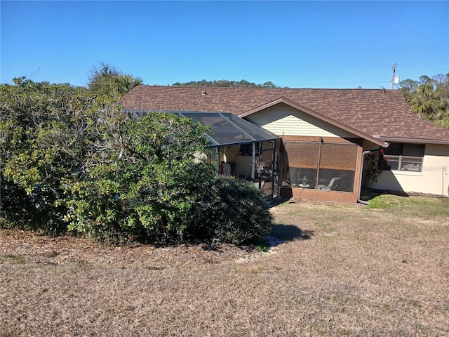 rear view of property with a lanai, a shingled roof, a lawn, and stucco siding