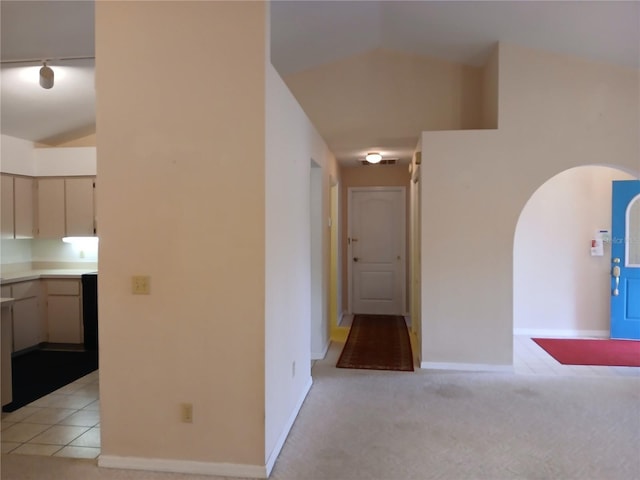 corridor featuring arched walkways, vaulted ceiling, baseboards, and light colored carpet