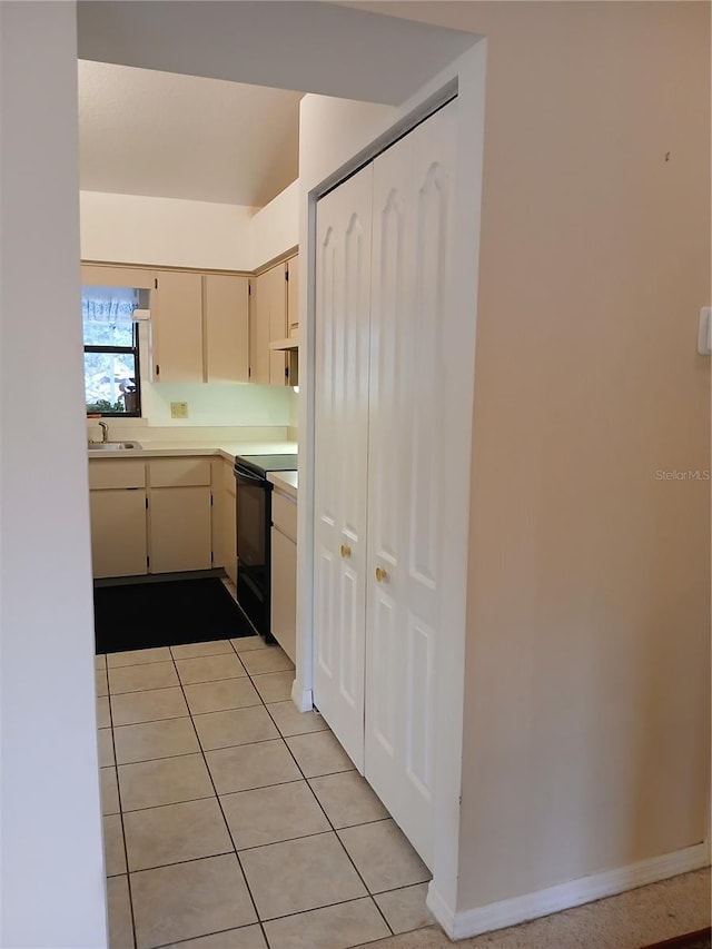 kitchen with light tile patterned floors, black / electric stove, light countertops, cream cabinetry, and a sink