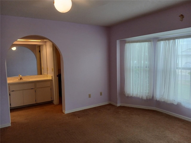 unfurnished bedroom with light carpet, baseboards, arched walkways, and a sink