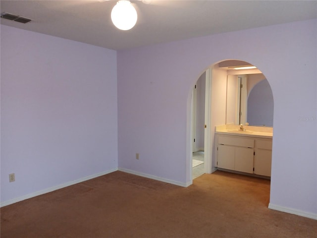 spare room with arched walkways, light colored carpet, a sink, visible vents, and baseboards